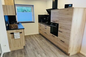 A modern kitchen with wooden cabinetry, a built-in oven, and a window with a view of greenery. - Holiday home in Pewsum with swimming pool (Pewsum)