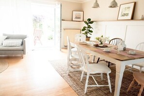 A dining area with a wooden table, white chairs, and a plant. - Edelhusen holiday home (Aurich)
