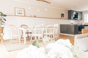 A modern kitchen with white cabinetry, pendant lights, and a dining area with white chairs. - Edelhusen holiday home (Aurich)
