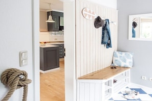 A room with a wooden bench, a wall-mounted coat rack, and a door leading to a kitchen. - Edelhusen holiday home (Aurich)