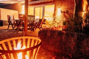 A patio area with a fire pit, outdoor seating, and a brick building in the background. - Edelhusen holiday home (Aurich)