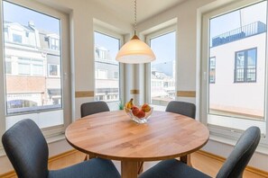 A round wooden table with four chairs, a hanging light fixture, and a fruit bowl on the table. - Apartment building Sandperle (Norderney)