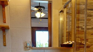 A bathroom with a white toilet, a wooden vanity with a sink, a glass shower enclosure, and a small trash bin. - Bianca Two Bedroom Apartment (Thessaloniki)