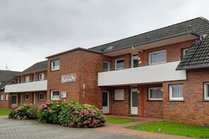 A brick building with a balcony, a sign indicating a restaurant, and a well-maintained garden. - Holiday apartment with 2 bedrooms (Borkum, Deutschland)