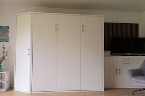A room with a white wardrobe, a flat-screen TV, and a grey chair. - Holiday apartment with 2 bedrooms (Borkum, Deutschland)