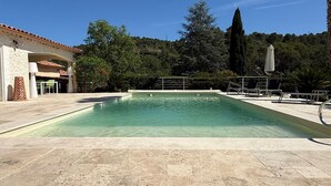 Una piscina con bordo in pietra, circondata da alberi e un edificio con tetto in tegole.