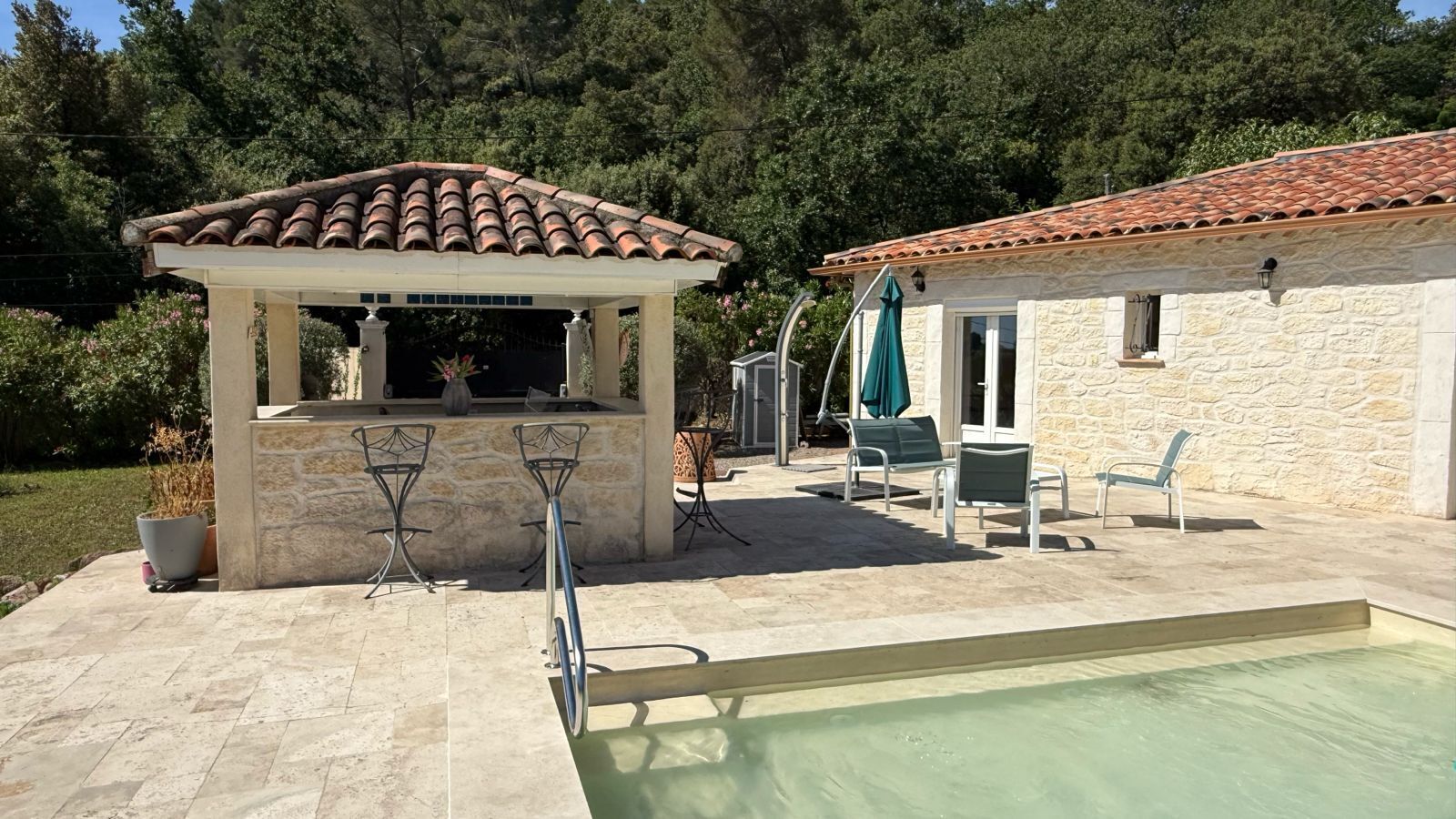 Un espace aménagé au bord de la piscine, doté d’une pergola, de sièges extérieurs et d’un bâtiment en pierre.