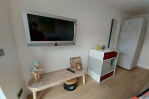 Ein Zimmer mit an der Wand montiertem Fernseher, einer Bank mit einer Figur, einem kleinen Tisch mit einem Schild und einem Schrank mit Schubladen.