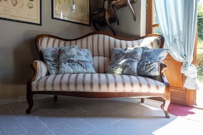 A striped sofa with floral cushions in a room with a tiled floor and framed botanical prints on the wall.