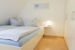 A bedroom with a bed, pillows, a bedside table with a lamp, and a framed picture on the wall. - Apartment building Sandperle, Apartment 4 (Norderney)