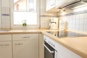 A kitchen with a window, white cabinets, a stove, and a coffee maker. - Apartment building Sandperle, Apartment 4 (Norderney)