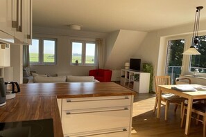 A modern kitchen with a wooden countertop, white cabinetry, and a dining area with a table and chairs. - Sea view in the Emma holiday home in Arngast (Varel-Dangast)