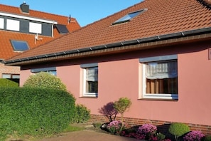 Ein rosafarbenes Haus mit Ziegeldach, einem kleinen Garten und blauem Himmel.