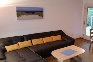 Ein Wohnzimmer mit einer schwarzen Couch, gelben Kissen, einem Holztisch und einem Bild mit einer Strandansicht an der Wand.