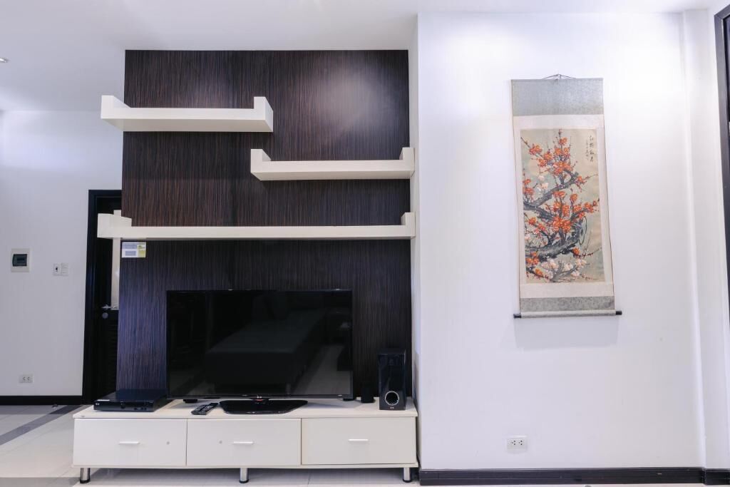 A modern living room with a flat-screen TV, a white entertainment unit, and a traditional artwork on the wall.