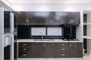 A modern kitchen with dark wood cabinets, a stainless steel sink, and a built-in oven. - Le Domaine De Cocodo Hotel (Thuan Hoa)