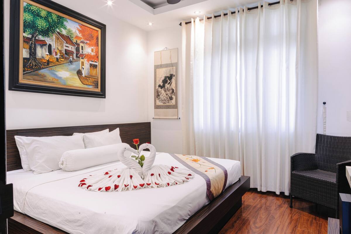 Un cuarto de hotel con una cama bien hecha, un cuadro en la pared y una silla.