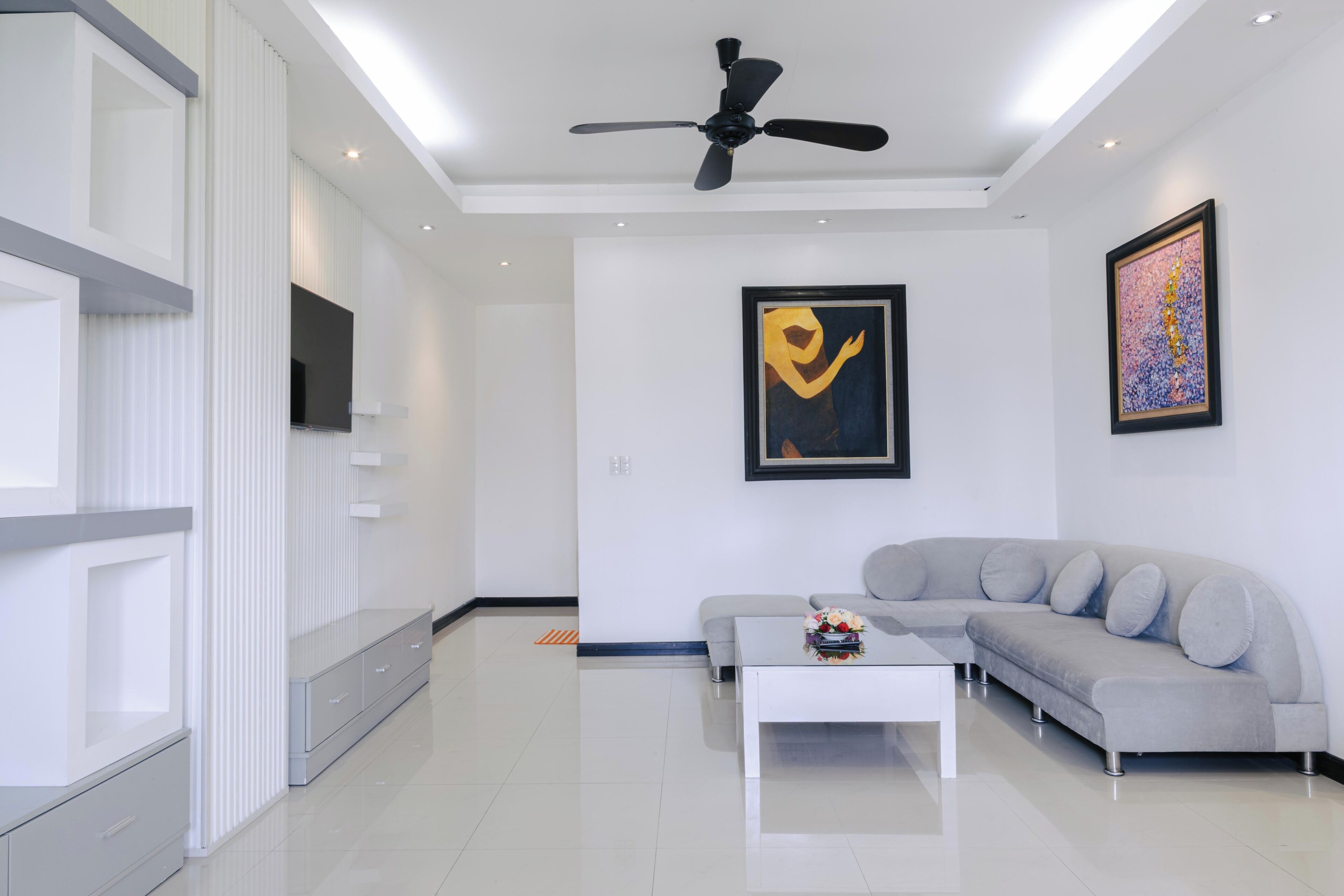 A modern living room with a ceiling fan, a grey sectional sofa, a white coffee table, and artwork on the walls.