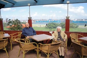 Two people seated at wicker tables with a view of a marina and boats in the background. - "Studio" in the "White House Varwig" (Nebel\/Süddorf)
