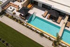 Ein Pool auf dem Dach mit Liegestühlen und Sonnenschirmen, umgeben von einer Steinmauer und einer Schachbrett-Fliesenbordüre.