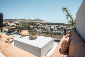 Eine Terrasse mit einer Couch, einem Tisch und einem Stuhl, mit Blick auf eine Stadt mit Gebäuden und Hügeln.