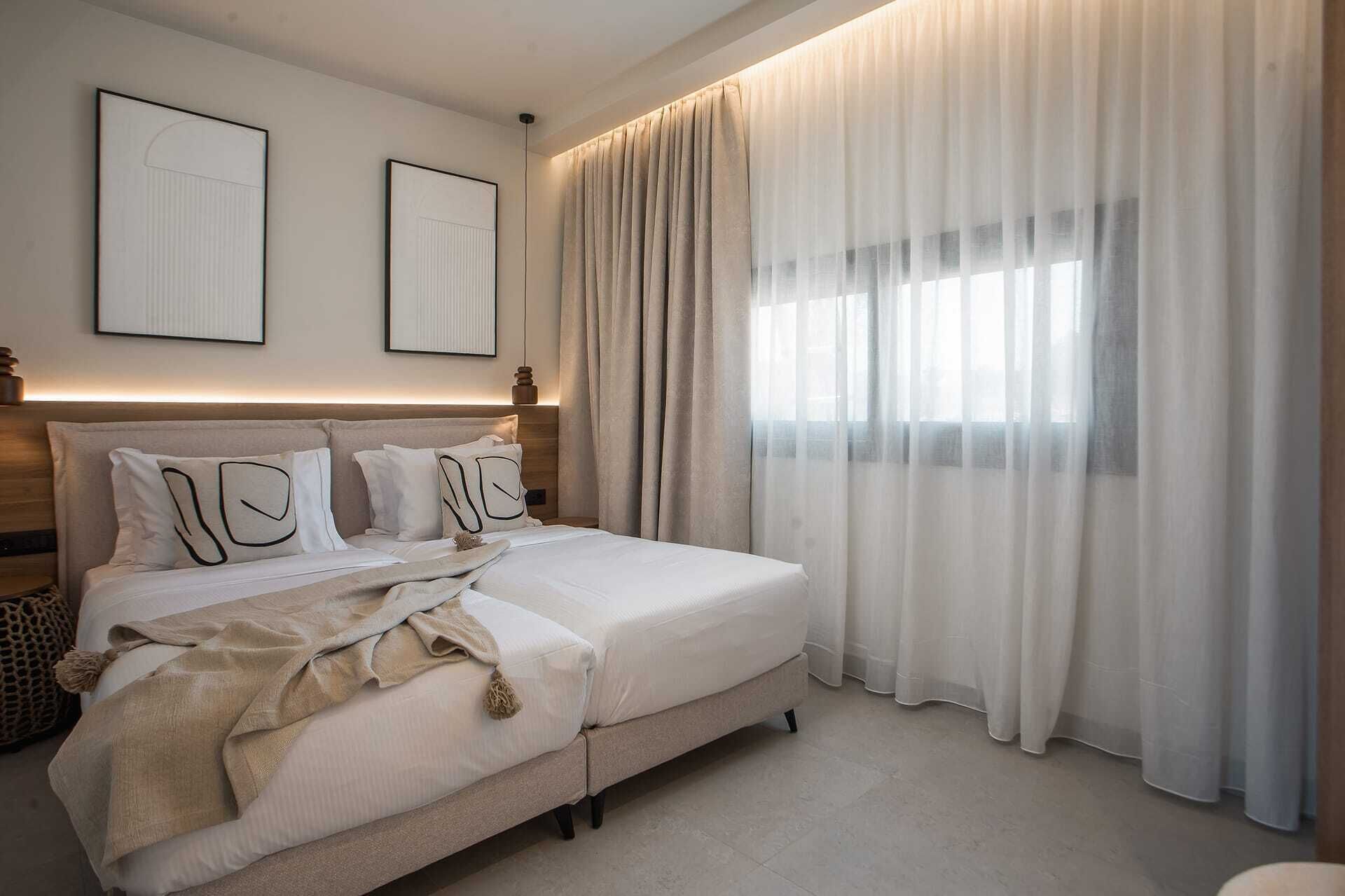 Een slaapkamer met een bed, twee kunstwerken in lijsten aan de muur en dunne gordijnen.