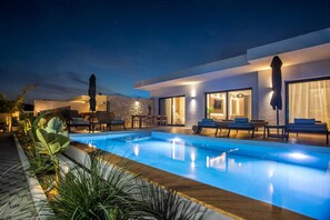 A modern pool area with lounge chairs and a stone wall. - Celeste Luxury Villas | Villa Gea, Villa (Rhodes)
