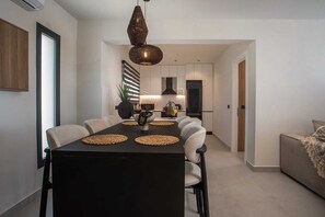 Et moderne spiseområde med et sort bord, vævede servietringe og en unik vævet pendel.