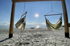 Een hangmat schommelset op een zanderig strand, met een heldere lucht en zichtbare zon.
