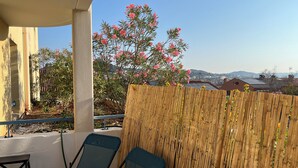 A covered patio with two blue chairs, a bamboo fence, and pink flowering plants. - Lou Cri-Cri Apartment in Hyères-les-Palmiers on Montée de Costebelle (Hyères)