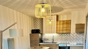 A modern living room with a sofa, a coffee table, and a dining area with a kitchen in the background. - Lou Cri-Cri Apartment in Hyères-les-Palmiers on Montée de Costebelle (Hyères)