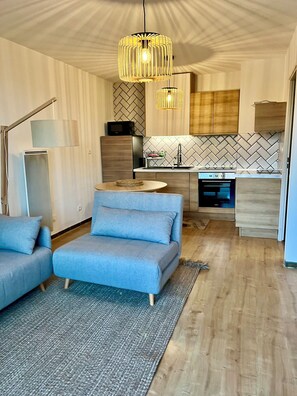 A modern living room with a sofa, a coffee table, and a dining area with a kitchen in the background. - Lou Cri-Cri Apartment in Hyères-les-Palmiers on Montée de Costebelle (Hyères)