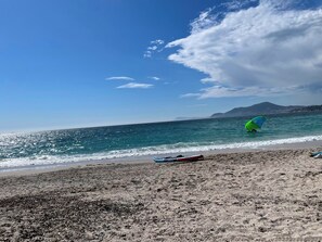 Ein Strand mit blauem Himmel, einem Gewässer und einem entfernten Berg.