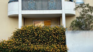 A multi-story building with balconies, a concrete planter with yellow flowers, and a small tree. - Lou Cri-Cri Apartment in Hyères-les-Palmiers on Montée de Costebelle (Hyères)