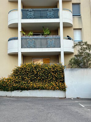 A multi-story building with balconies, a concrete planter with yellow flowers, and a small tree. - Lou Cri-Cri Apartment in Hyères-les-Palmiers on Montée de Costebelle (Hyères)