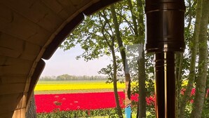A cozy room with a wooden bench, a window with a view of a field of red flowers, and a wood stove. - Finnish kota with a private wood-fired barrel sauna (Slootdorp)