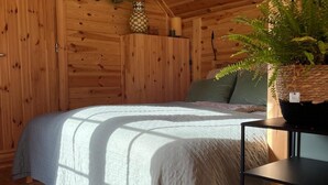 A wooden cabin bedroom with a bed, a nightstand, a potted plant, and a wall-mounted shelf. - Finnish kota with a private wood-fired barrel sauna (Slootdorp)