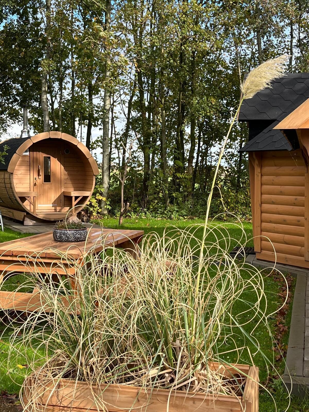 Una cabaña de madera con una estructura en forma de barril, una terraza de madera y un jardín con pastos altos.