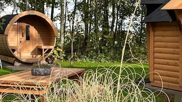 Una cabaña de madera con una estructura en forma de barril, una terraza de madera y un jardín con pastos altos.