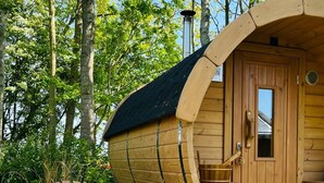 A wooden boat-shaped cabin with a bench and a table outside, surrounded by trees. - Finnish kota with a private wood-fired barrel sauna (Slootdorp)