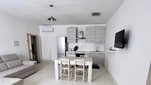 Un salon moderne comprenant un canapé, une table à manger avec des chaises, un coin cuisine avec des placards et un téléviseur fixé au mur.