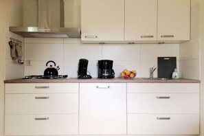 Eine Küche mit weißen Schränken, einem Gasherd, einer Kaffeemaschine und einer Obstschale.