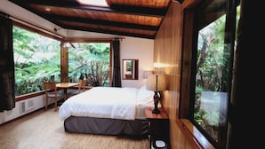 A bedroom with a bed, bedside table, lamp, and a window with a view of greenery.