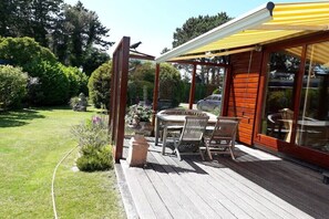 Eine Holzterrasse mit überdachter Sitzecke, einem Steingartenbeet und Blick auf den umliegenden Garten.