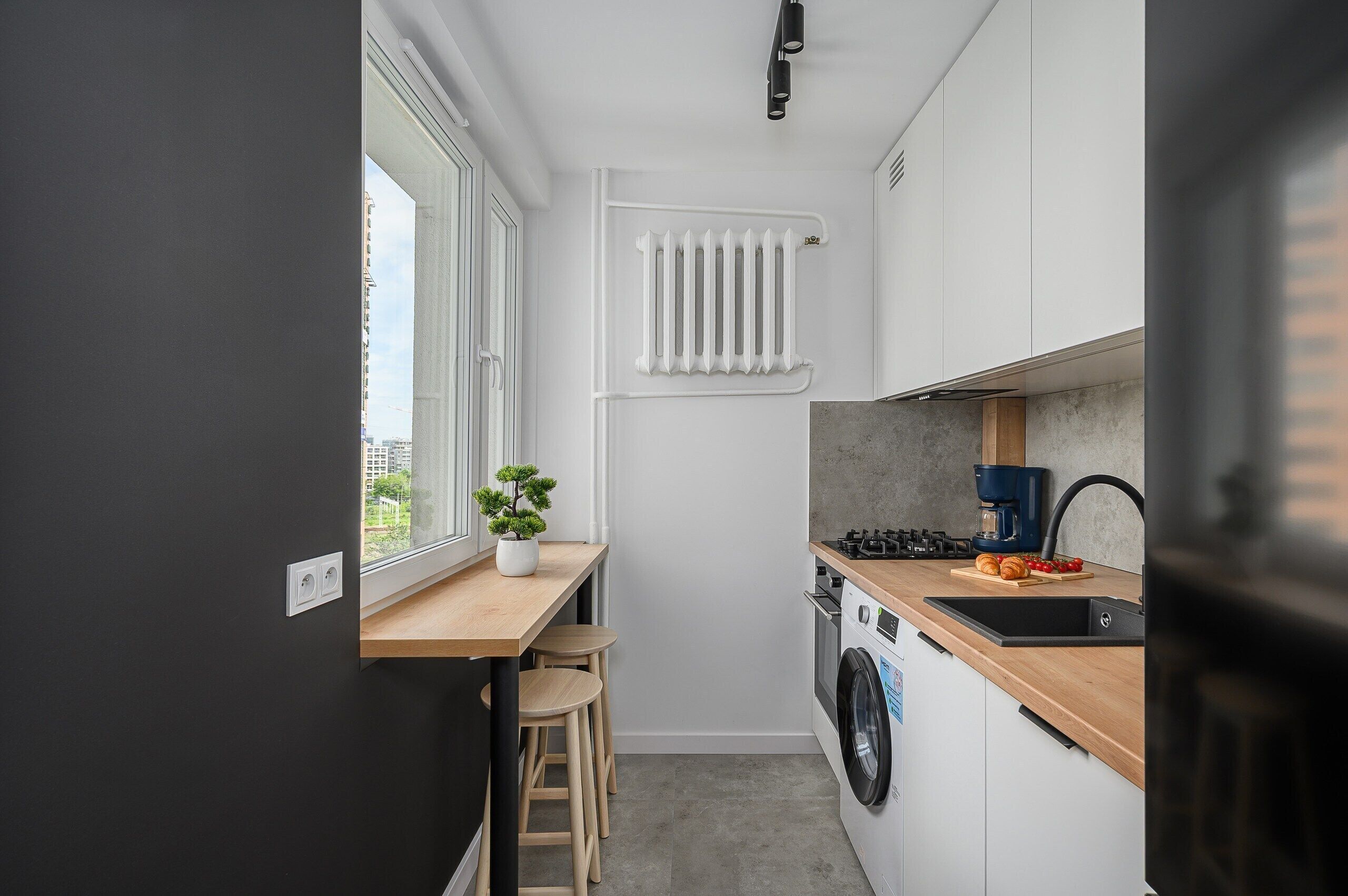 A compact kitchen with a built-in washer, a window, and a radiator.