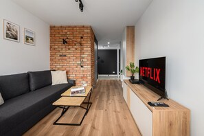 Una sala de estar moderna con una pared de ladrillo decorativa, un sofá, una mesa de centro, un televisor y un control remoto.