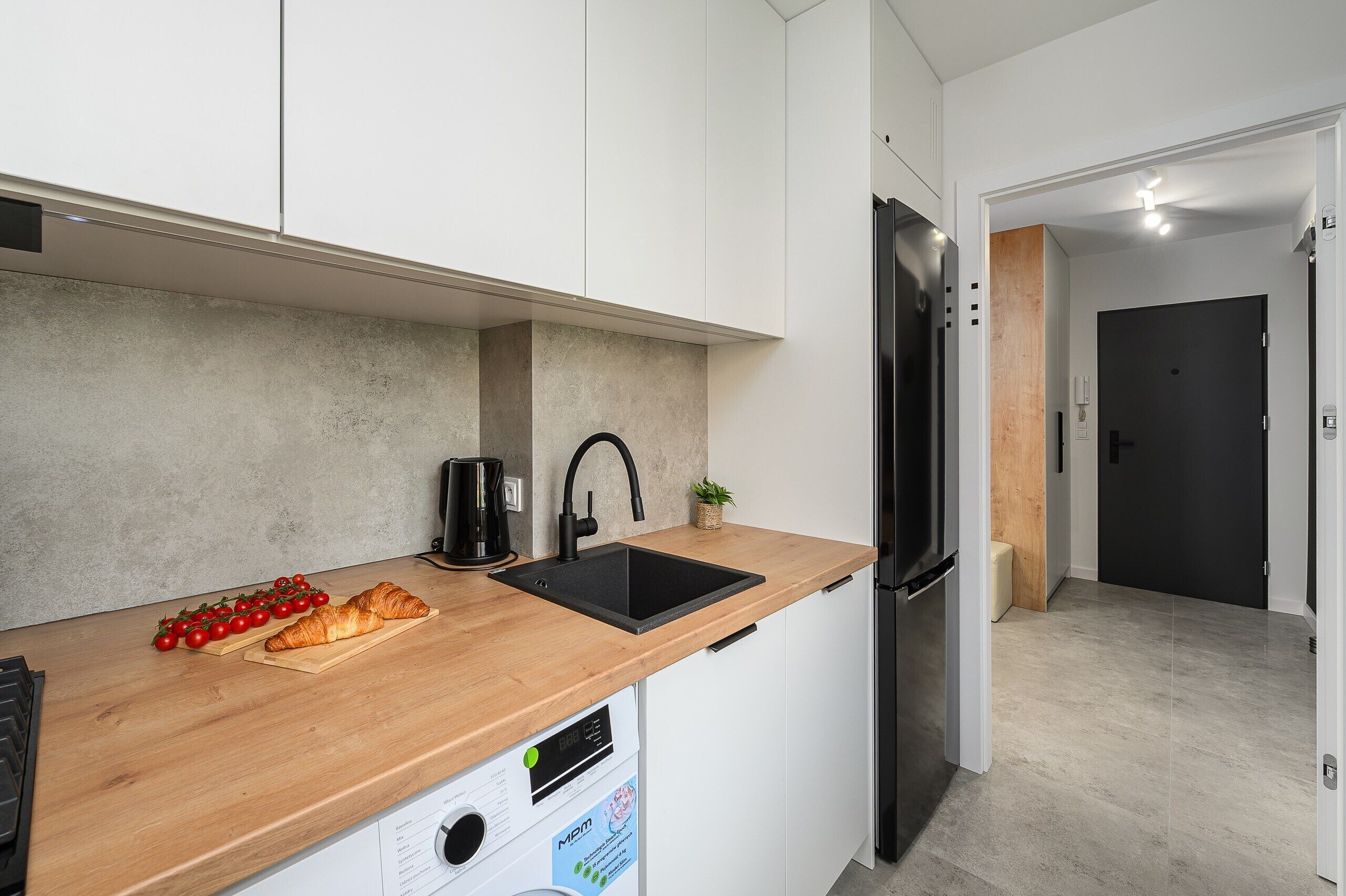 Una cucina moderna con un piano di lavoro in legno, un lavello nero e un frigorifero in acciaio inossidabile.