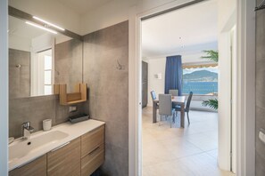 Ein modernes Badezimmer mit einem großen Spiegel, einem Waschbecken und Holzschränken. Es führt zu einem Balkon mit Esstisch und Stühlen, der einen schönen Ausblick bietet.