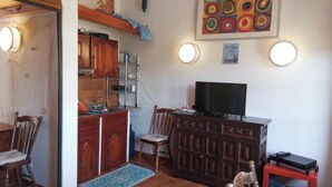 A room with a wooden dining table, chairs, a TV on a stand, a cabinet, and a painting on the wall. - Villetta Mannucciu – 1-Bedroom Apartment with Ocean View in Rena Majore (Rena Majore)