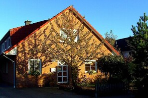 Ein Ziegelhaus mit rotem Dach, ein Baum im Vordergrund und ein klarer, blauer Himmel.
